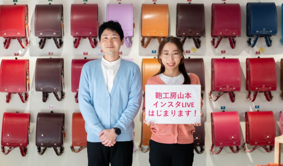 カラフルなランドセルの前で笑顔のスタッフの写真