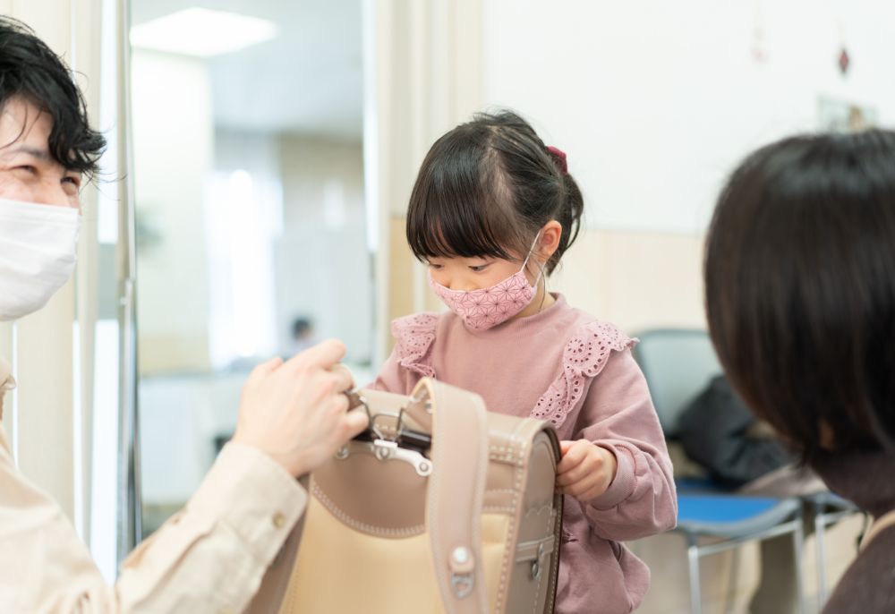 女の子に水色のランドセルを背負うのを手伝うスタッフの写真