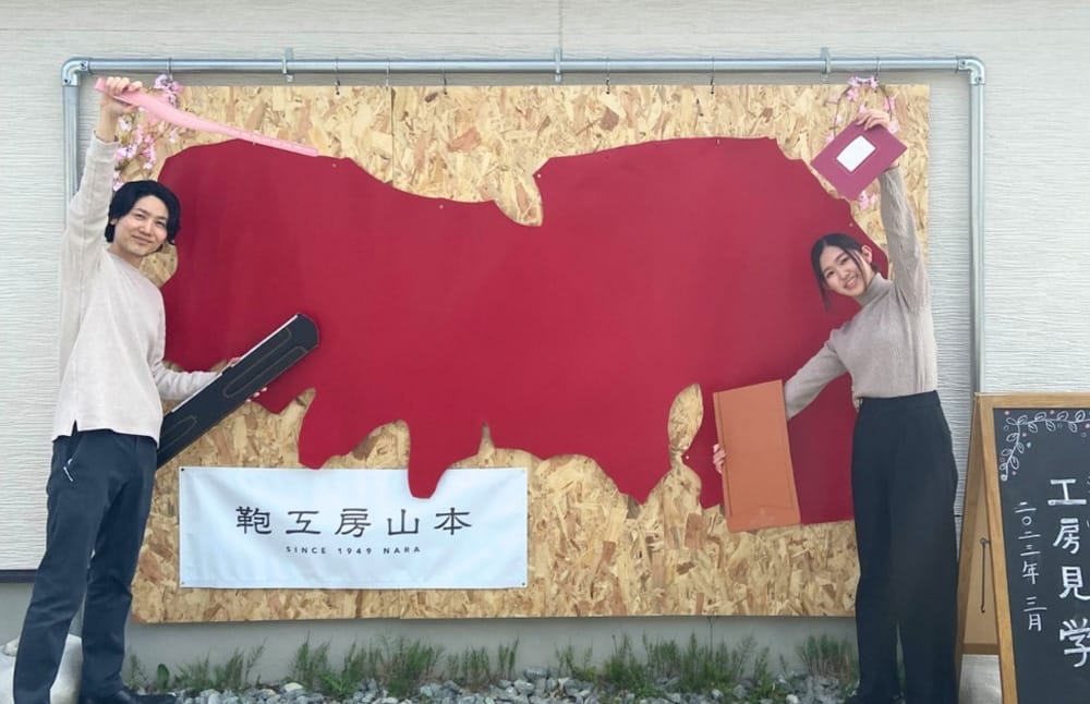 大きな牛革が壁に展示され両橋でポーズをとる工房スタッフの写真