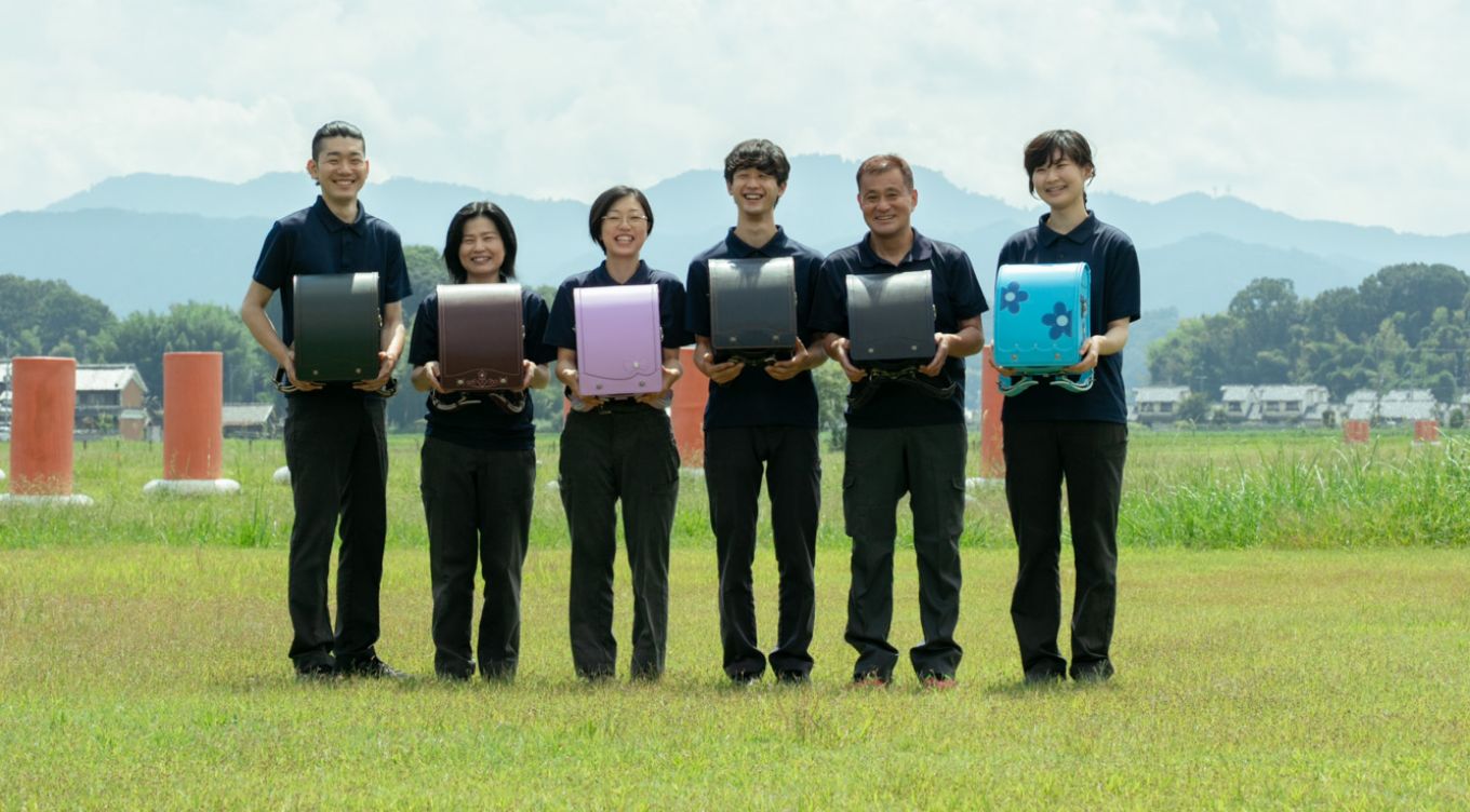 ランドセルを手に笑顔の工房スタッフ6人の写真
