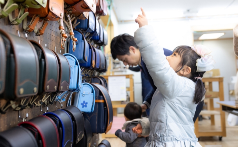 様々なカラー、デザインのランドセルの中から、ひとつを選んで指差す女の子