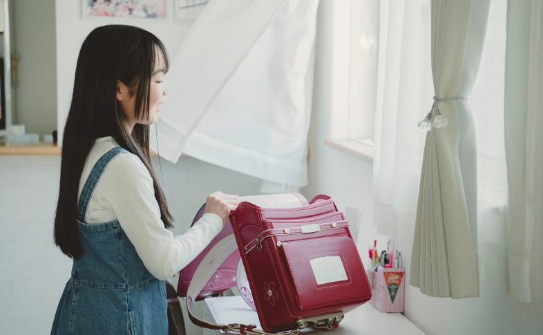 ローズピンクのランドセルを机の上で開く少女