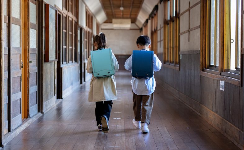 学校を歩く緑のランドセルを背負う女の子と男の子